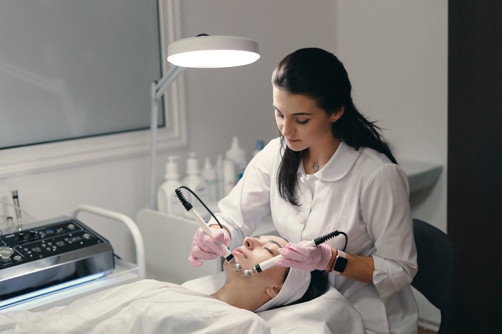 Model with closed eyes and hand's of doctor. Rejuvenating facial treatment. Model getting lifting therapy massage in a beauty SPA salon. Cosmetological clinic, procedure.